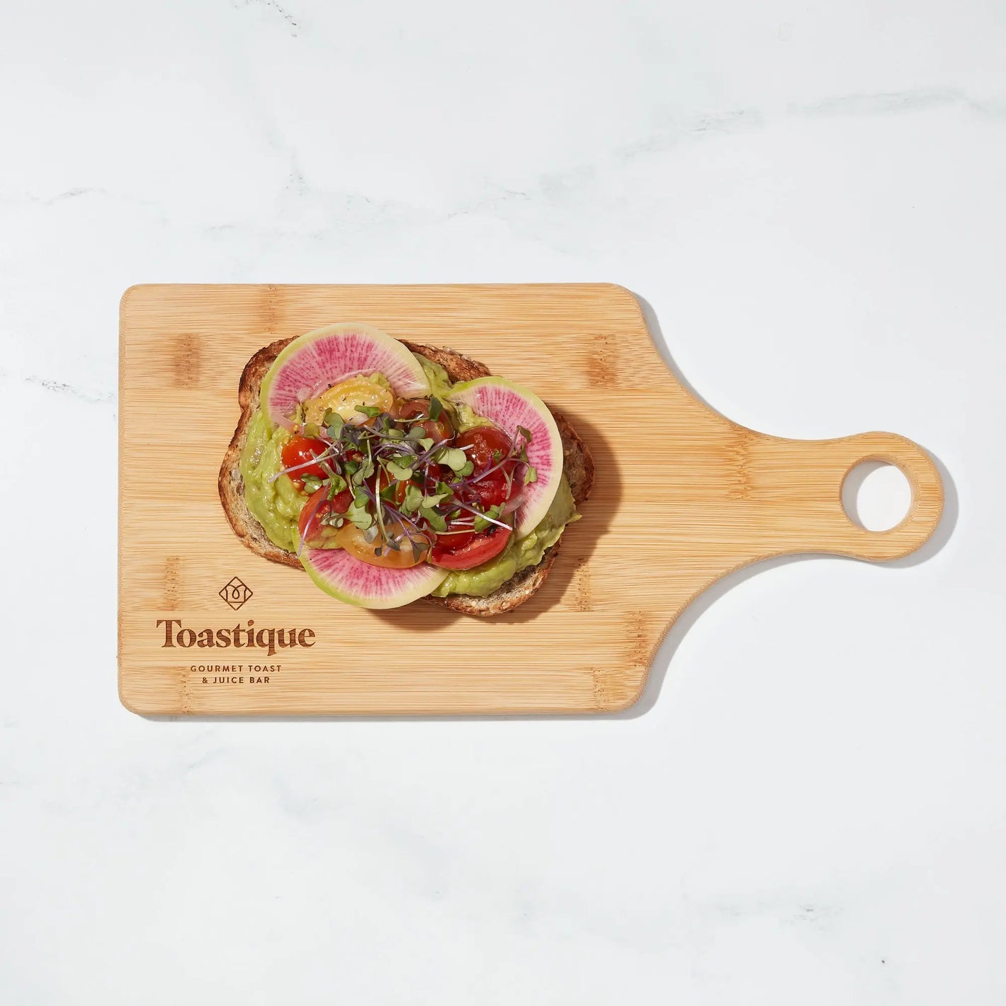 Avocado Smash toast with watermelon radish, marinated tomatoes, and microgreens on a Toastique board