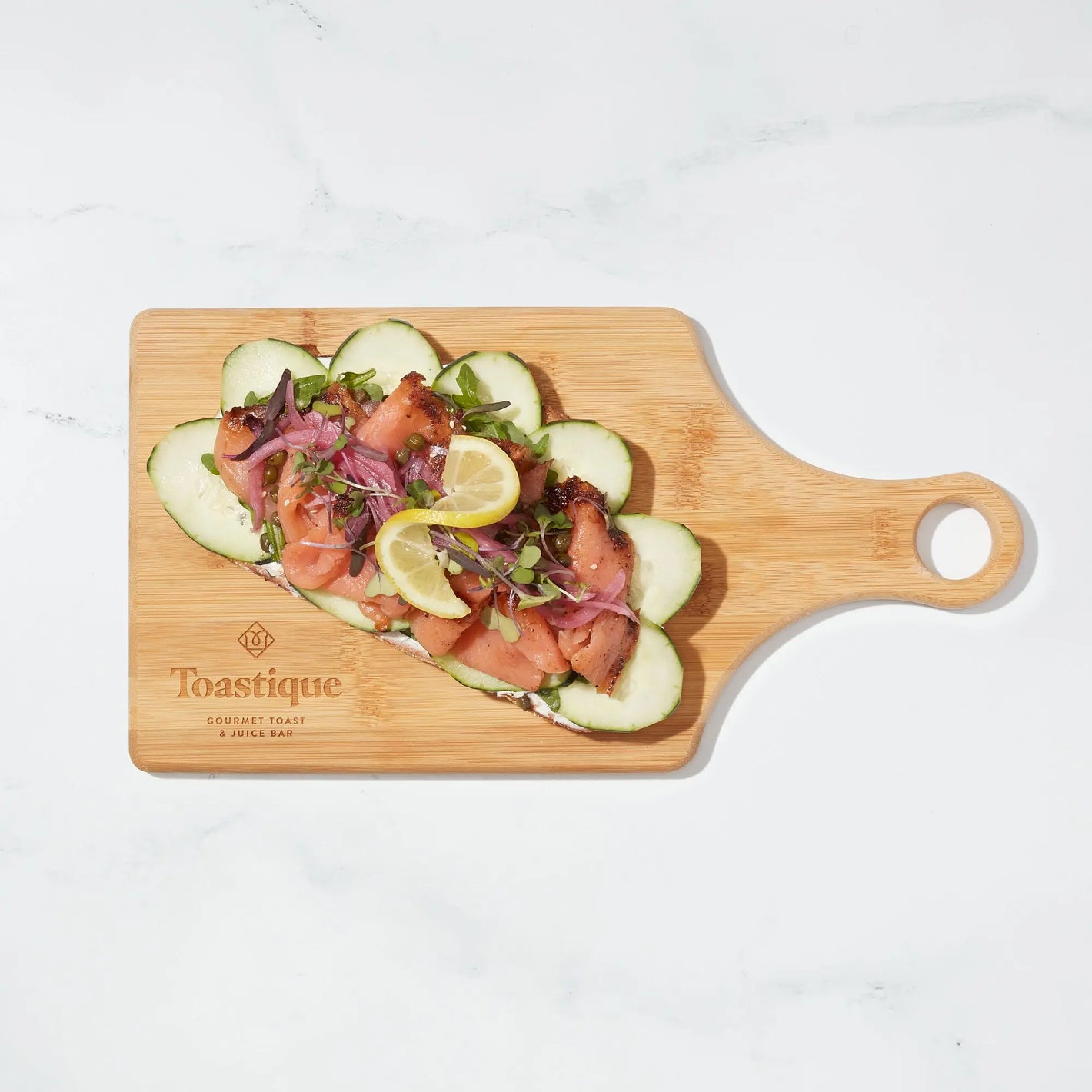 Smoked Salmon toast with cucumber, pickled onion, and a lemon twist on a Toastique board